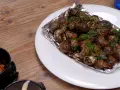 Caracoles con mantequilla y perejil, servidos en papel de aluminio sobre un plato blanco, junto a un cuenco con salsa.