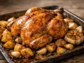 Pollo troceado al horno jugoso, dorado y crujiente, acompañado de patatas asadas y ajos enteros.