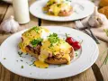 Huevos Benedictinos en plato blanco con salsa holandesa, perejil y chiles rojos.
