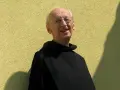 Uśmiechnięty starszy mężczyzna w czarnym habicie, z okularami na nosie, wygląda jak pobożna dewota.