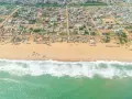 Widok z lotu ptaka na plażę i zabudowania w Kotonu, stolicy Beninu. Zielone morze z falami obmywa piaszczysty brzeg, za którym rozciąga się miasto.