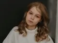 Młoda dziewczyna z burzą brązowych włosów, w białym golfie, zamyślona. Zastanawia się, jak przeprosić dziewczynę, by naprawić błąd.