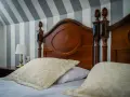Eleganckie łóżko z drewnianym zagłówkiem i ozdobnymi poduszkami. Ciekawe, ile wynosi ryczałt za nocleg w takim miejscu?