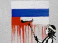 Dziecko w wianku maluje wałkiem czerwoną farbę na fladze Rosji.