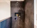 Ducha moderna con tabique de obra y muro de cristal. Incluye alcachofa de lluvia, grifería empotrada y nicho con botes de champú.