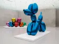 Un chien ballon bleu iconique de Jeff Koons, reflétant l'espace d'exposition. D'autres sculptures de ballons colorés sont visibles en arrière-plan.