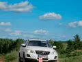 Białe Volvo XC60 T6 jedzie po piaszczystej drodze wśród zieleni, pod błękitnym niebem z chmurami.