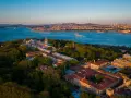 Aerial view of the Topkapi Palast complex, nestled amongst lush greenery, with the Bosphorus Strait and Istanbul skyline in the background.