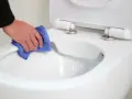 Main propre avec un chiffon bleu, nettoyant le bord d'un wc avec bride ou sans bride.