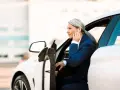 Elegancka kobieta w garniturze wsiada do białego auta. To jej auto na abonament, idealne do biznesowych podróży.