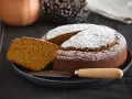 Bizcocho de calabaza esponjoso y dorado, espolvoreado con azúcar glas. Una rebanada muestra su interior húmedo y aromático.