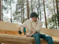 Mężczyzna buduje altanę, skręcając drewniane elementy wkrętarką. To pierwszy krok, jak zrobić drzwi do altany.