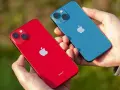Dwie dłonie trzymają dwa telefony: czerwony i niebieski iPhone 13 mini. Aparat obu modeli jest widoczny.