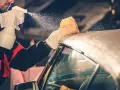 A person in gloves sprays a convertible car's fabric top with cleaning solution, then wipes it with a sponge. This is how you wash a convertible car.