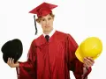 Studente universitario lavoratore con toga e cappello da laureato, tiene in mano un cappello nero e un casco giallo, indeciso sul futuro.