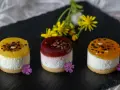 Efektowne ciasto bez pieczenia: trzy mini deserki z galaretką, kremem i owocami, ozdobione kwiatami i czekoladą.