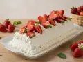 Delizioso rotolo panna e fragole, ricoperto di panna montata e fragole fresche, con fragole in un cestino sullo sfondo.
