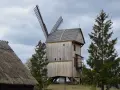 Wiatrak w skansenie Kaszuby, drewniany, z widocznymi skrzydłami i strzechą na dachu.