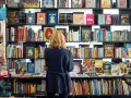 Donna bionda in libreria, circondata da scaffali pieni di libri colorati. Un'atmosfera di lavoro e scoperta tra le pagine.