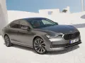 Szary sedan Skoda Superb, segment d, zaparkowany na tle nowoczesnej architektury.