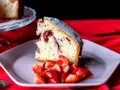 Un trozo de bizcocho de fresa esponjoso, espolvoreado con azúcar glas, servido con fresas frescas cortadas en un plato rosa.