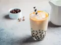 Erfrischendes Bubble Eis mit Tapiokaperlen und Eiswürfeln in einem Glas, daneben eine Schale mit dunklen Perlen.