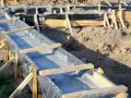 Fundamenty wylewane w wykopie, zabezpieczone folią, z drewnianym szalunkiem. Widać ziemię i przygotowania do dalszych prac budowlanych, uwzględniające głębokość przemarzania gruntu wzór.