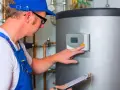 Technik w niebieskim kombinezonie reguluje panel sterowania bojlerem, dbając o sprawne działanie centralnego ogrzewania.