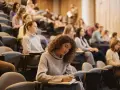 Junge Frau mit Locken schreibt konzentriert in ein Notizbuch, während sie an ihrem Erasmus Studium teilnimmt.