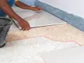 Hand legt neue Fliesen auf alte, um die Bodenfliesen zu erneuern.