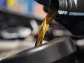 Goldfarbenes Motoröl fließt aus einem schwarzen Behälter in einen dunklen Trichter.