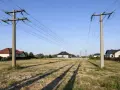 Dwa słupy energetyczne z przewodami linii wysokiego napięcia 110 kV, nad pustą działką z domami w tle. Zachowanie bezpieczna odległość od linii wysokiego napięcia 110 kv jest kluczowe.