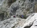 Dwóch turystów pokonuje via ferraty w Dolomitach, wspierając się na stalowej linie.
