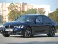 Ciemnoniebieskie BMW 318d z polskimi tablicami rejestracyjnymi stoi na tle budynków i drzew.
