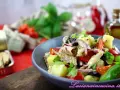 Un'insalata pantesca colorata con patate, pomodorini, olive, cipolla rossa e pesce, guarnita con basilico fresco.