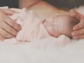 Delikatne otulenie noworodka w różowy kocyk, ręce rodzica czule obejmujące główkę. Idealne jak układać dziecko do snu gdy ulewa.
