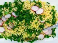 En fräsch bulgursallad med rädisor och färska örter, serverad på en vit tallrik med en sked.