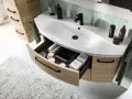 Aménagement salle de bain moderne avec lavabo blanc, robinetterie noire et tiroirs en bois clair organisés.