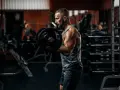 Mężczyzna ćwiczy biceps z ciężarem. W tle siłownia, sprzęt i inny ćwiczący.