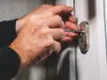Ręce z wytrychem próbują otworzyć zatrzaśnięte drzwi.