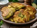 Goldbraune zucchini puffer auf einem Teller, mit Kräutern und einem Dip im Hintergrund.