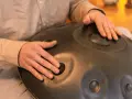 Dłonie grają na instrumencie typu hang drum, tworząc kojące dźwięki.