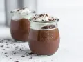 Zwei Gläser mit cremigem omas schokoladenpudding, gekrönt mit Schlagsahne und Schokostreuseln.