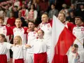 Polska drużyna piłki ręcznej z flagą narodową. Młodzi zawodnicy i dzieci w strojach biało-czerwonych.