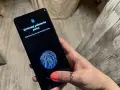 Dłoń z telefonem, na ekranie skaner linii papilarnych i komunikat "Zmieniaj położenie palca". To jak próba ucieczki z cyfrowego więzienia, niczym **jailbreak**.