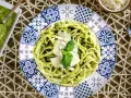 Pasta al pesto servida en plato decorado, con salsa de pesto y queso rallado al lado.
