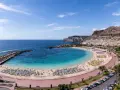 Słoneczna plaża z turkusową wodą i mnóstwem leżaków. W oddali klify i hotele, idealne gran canaria atrakcje dla każdego.