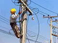 Elektryk w żółtym kasku pracuje na słupie energetycznym, podłączając przewody. Zastanawiasz się, ile kosztuje przyłącze elektryczne?