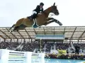 Un cavalier et son cheval s'envolent au-dessus d'une rivière lors d'un CSI Equitation. Le public applaudit dans les gradins.