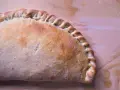 Złocisty calzone, pieczony na drewnianym tle, z charakterystycznym, zaplecionym brzegiem. Idealny na szybki posiłek.